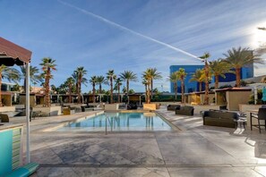 A pool area with lounge seating and palm trees, surrounded by modern buildings.