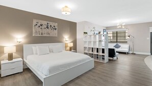 Ein modernes Schlafzimmer mit einem großen Bett, Nachttischen, einem weißen Kleiderschrank und einem Schreibtisch mit Stuhl.
