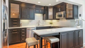 Une cuisine moderne avec des meubles de couleur sombre, un plan de travail blanc et des appareils électroménagers en acier inoxydable.