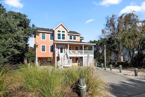 A two-story house with a balcony, surrounded by tall grass and trees.