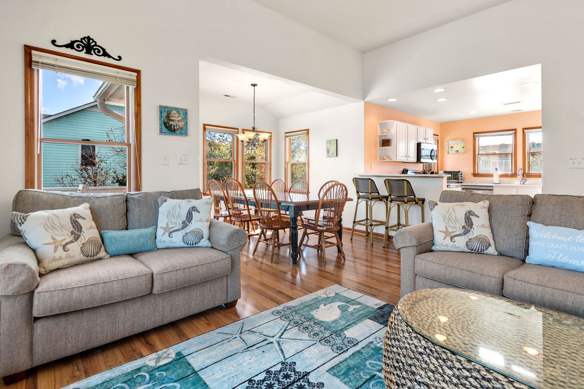 A spacious living room with two sofas, a dining table, and chairs. A kitchen is visible in the background with modern appliances.