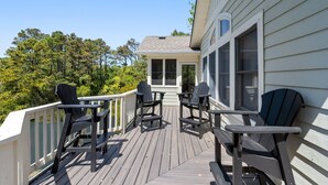 A wooden deck with outdoor seating and a view of trees. - Ocean Escape: Lakefront, Pool, Hot Tub, Game Room (Corolla)