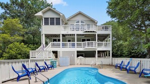A two-story building with a swimming pool, surrounded by blue chairs and a white fence. - Ocean Escape: Lakefront, Pool, Hot Tub, Game Room (Corolla)