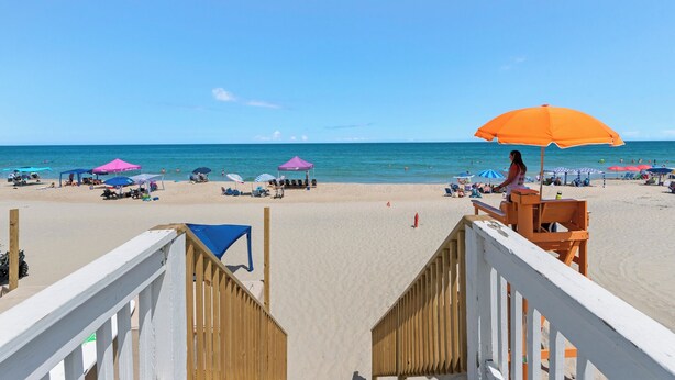 A beach with a wooden deck, beach umbrellas, and a lifeguard stand. - Ocean Escape: Lakefront, Pool, Hot Tub, Game Room (Corolla)