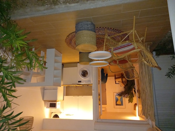 A kitchen with a microwave, a washing machine, and a hanging wicker chair.
