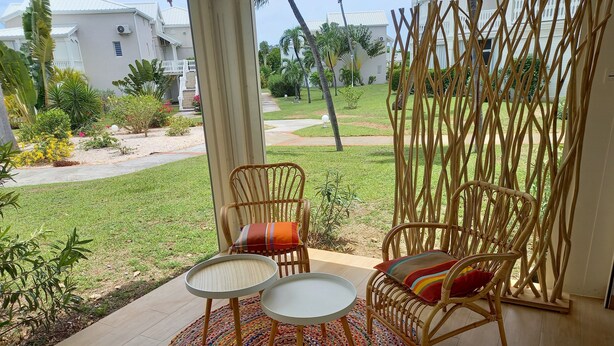 A patio with wicker chairs and a round table, overlooking a well-maintained garden and a white building in the background. - beautiful studio in st martin (Saint Martin)