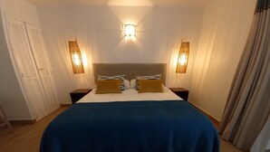 A bedroom with a large bed, two nightstands, a wall-mounted light fixture, and a door with louvered shutters. - beautiful studio in st martin (Saint Martin)