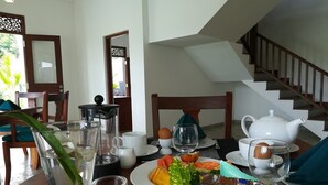 Een eettafel met eten, een theepot en een mand vol fruit.