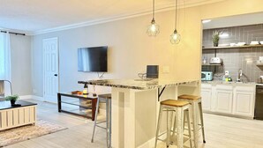 A modern kitchen with a marble countertop, two bar stools, a TV mounted on the wall, and a small island. - Spacious 4-Bedroom Condo in Downtown Atlanta (Atlanta)
