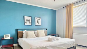 A bedroom with a bed, two bedside tables, a nightstand, a window with curtains, and two wall art pieces. - Spacious 4-Bedroom Condo in Downtown Atlanta (Atlanta)