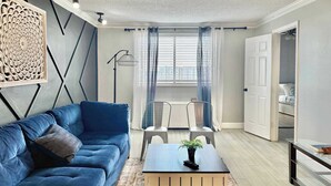A modern living room with a blue sofa, a small table with a plant, and a view of a bedroom through a door. - Spacious 4-Bedroom Condo in Downtown Atlanta (Atlanta)