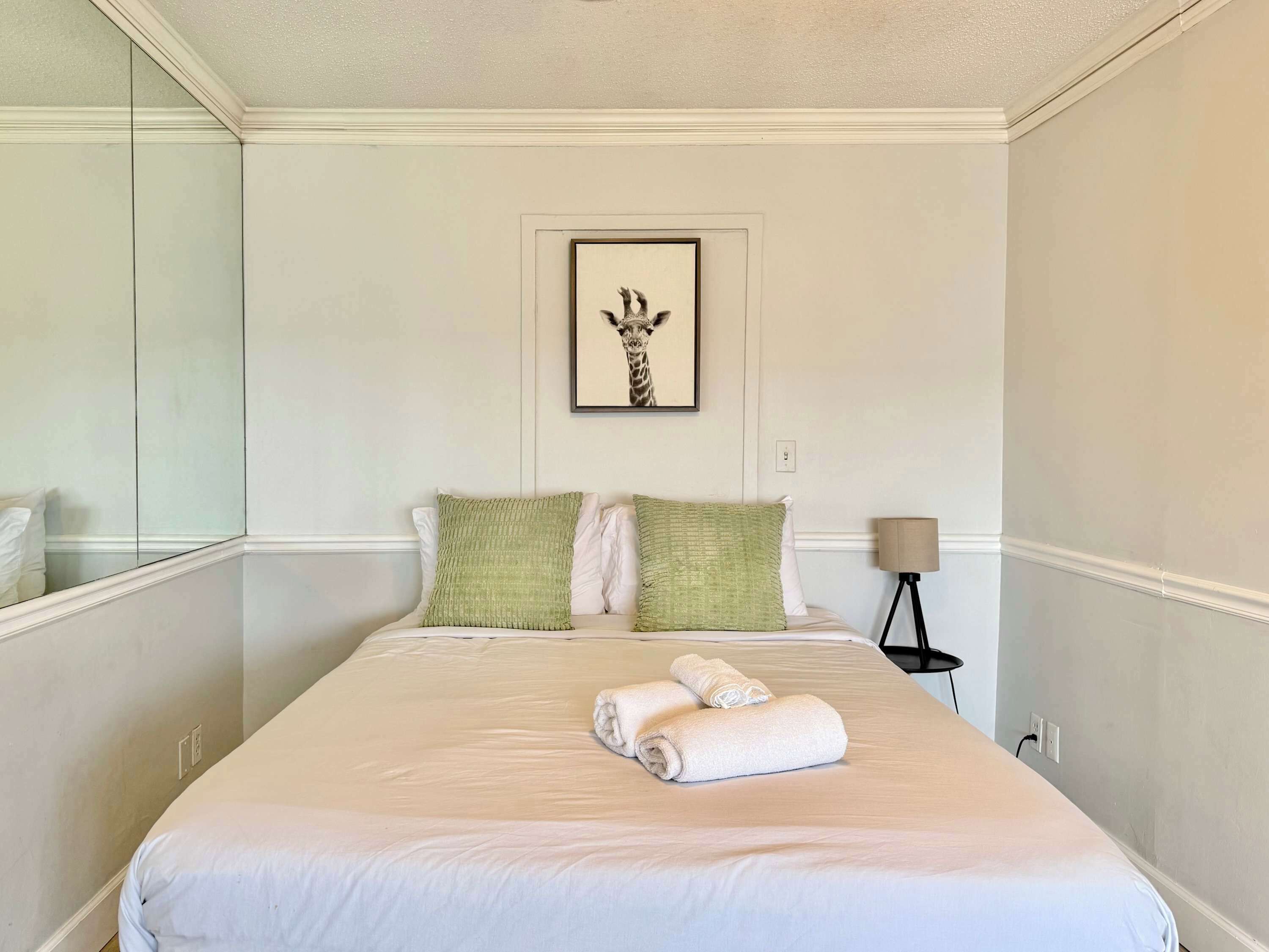 A neatly made bed with pillows, a framed picture on the wall, and a lamp on a side table.