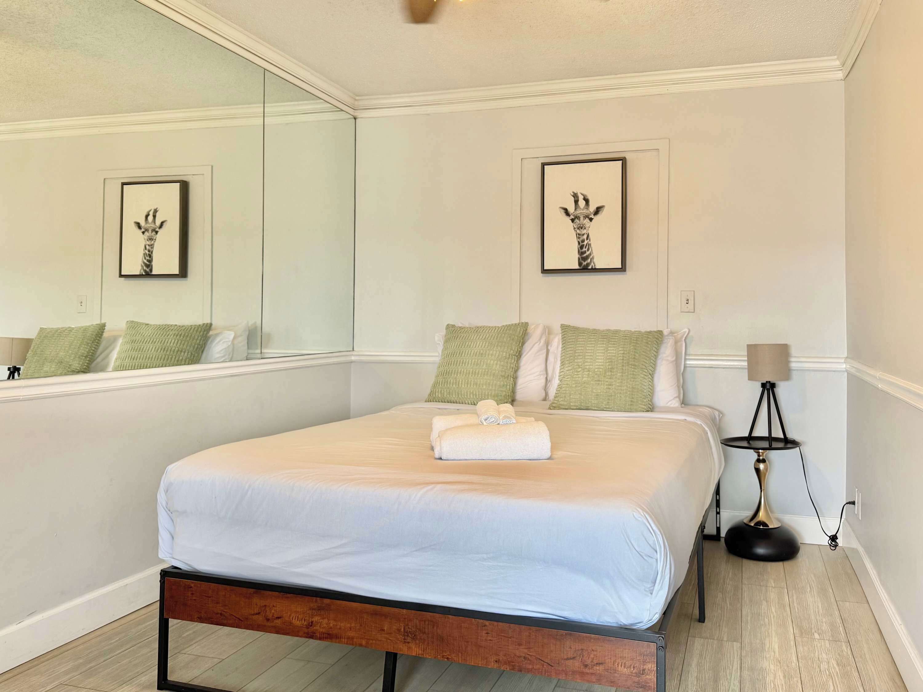 Een slaapkamer met een bed, kussens, een bedlampje en lijstjes met foto’s aan de muur.