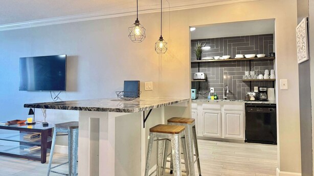 A modern kitchen with a marble countertop, two stools, a TV, and a dishwasher. - Spacious 4-Bedroom Condo in Downtown Atlanta (Atlanta)