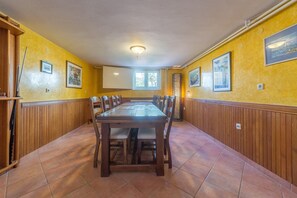 Un espace repas avec une longue table en bois et des chaises, des murs jaunes et un lambris en bois.