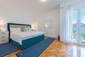Une chambre à coucher avec un lit, des tables de chevet, un miroir, une bouteille et une vue par la fenêtre.