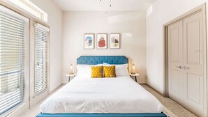 Une chambre à coucher avec un grand lit, une tête de lit bleue et une vue sur la ville grâce à de grandes fenêtres du sol au plafond.