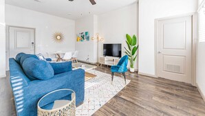 Un salon moderne avec un canapé bleu, un ventilateur de plafond, un téléviseur et une grande plante.
