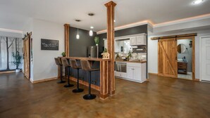 A modern kitchen with a central island, bar stools, pendant lighting, and a sliding barn-style door.