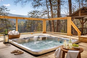 Un jacuzzi en una terraza de madera con vistas a árboles y montañas.