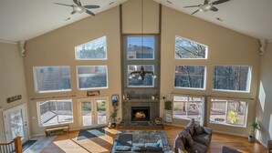 A spacious living room with a fireplace, large windows, and ceiling fans.