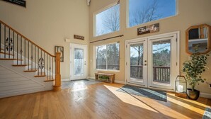 A spacious living area with a wooden staircase, a bench, and a large window overlooking a deck.