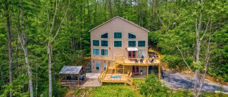 A two-story cabin with a deck, surrounded by dense forest.