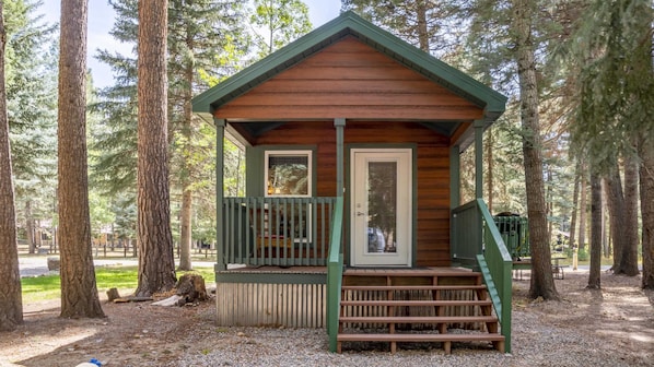 Eine kleine Holzhütte mit Veranda, umgeben von hohen Bäumen.