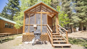 A small wooden cabin with a porch and a grill outside. - The Colorado Spruce Cabin #15 (Bayfield)