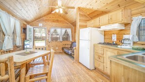 A wooden cabin with a kitchen area, including a refrigerator, stove, and dining table with chairs. - The Blue Spruce Cabin #16 (Bayfield)