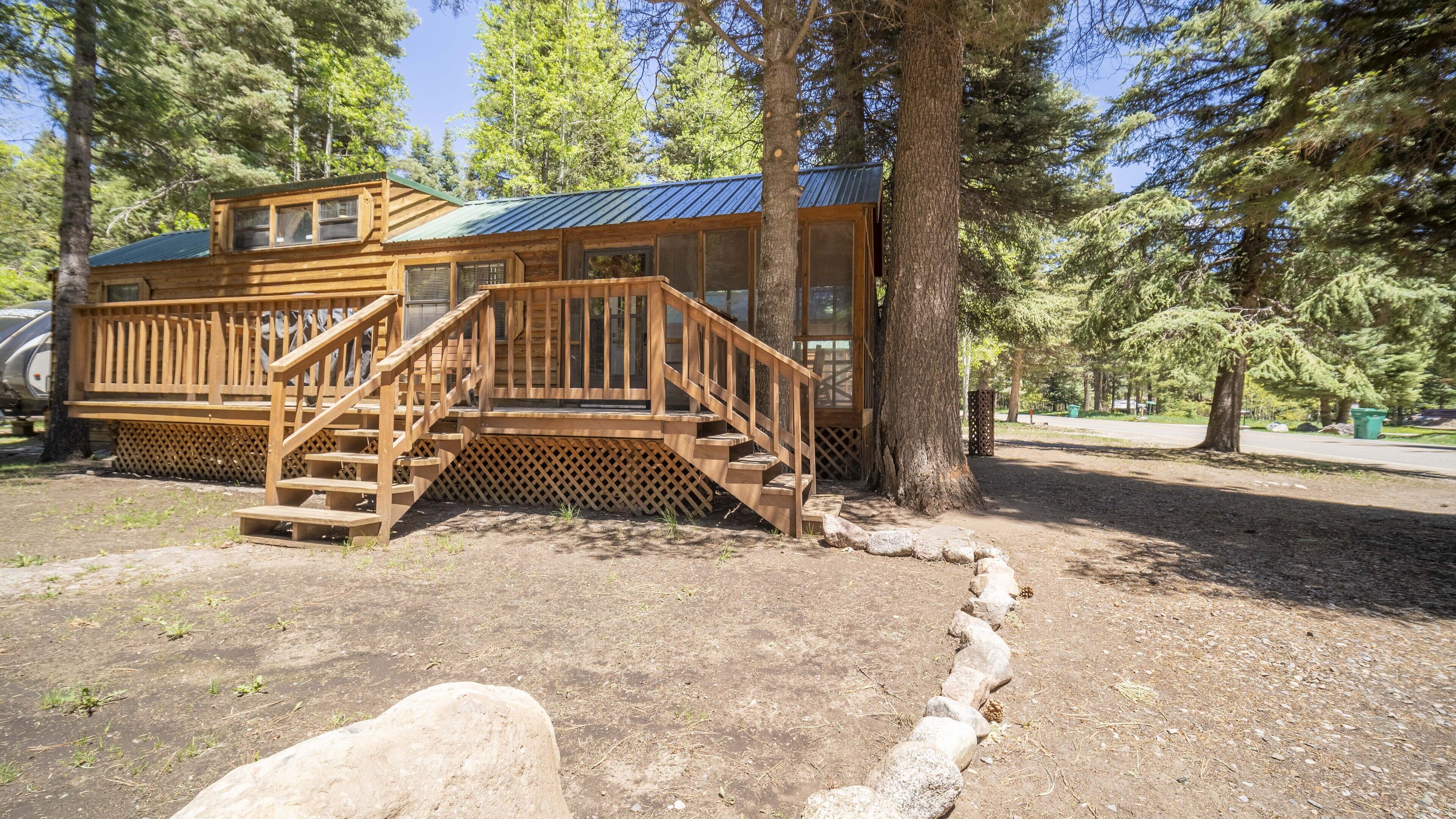 A wooden cabin with a deck and stairs, surrounded by trees.