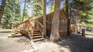 Une cabane en bois avec un escalier menant à une terrasse, entourée d’arbres.