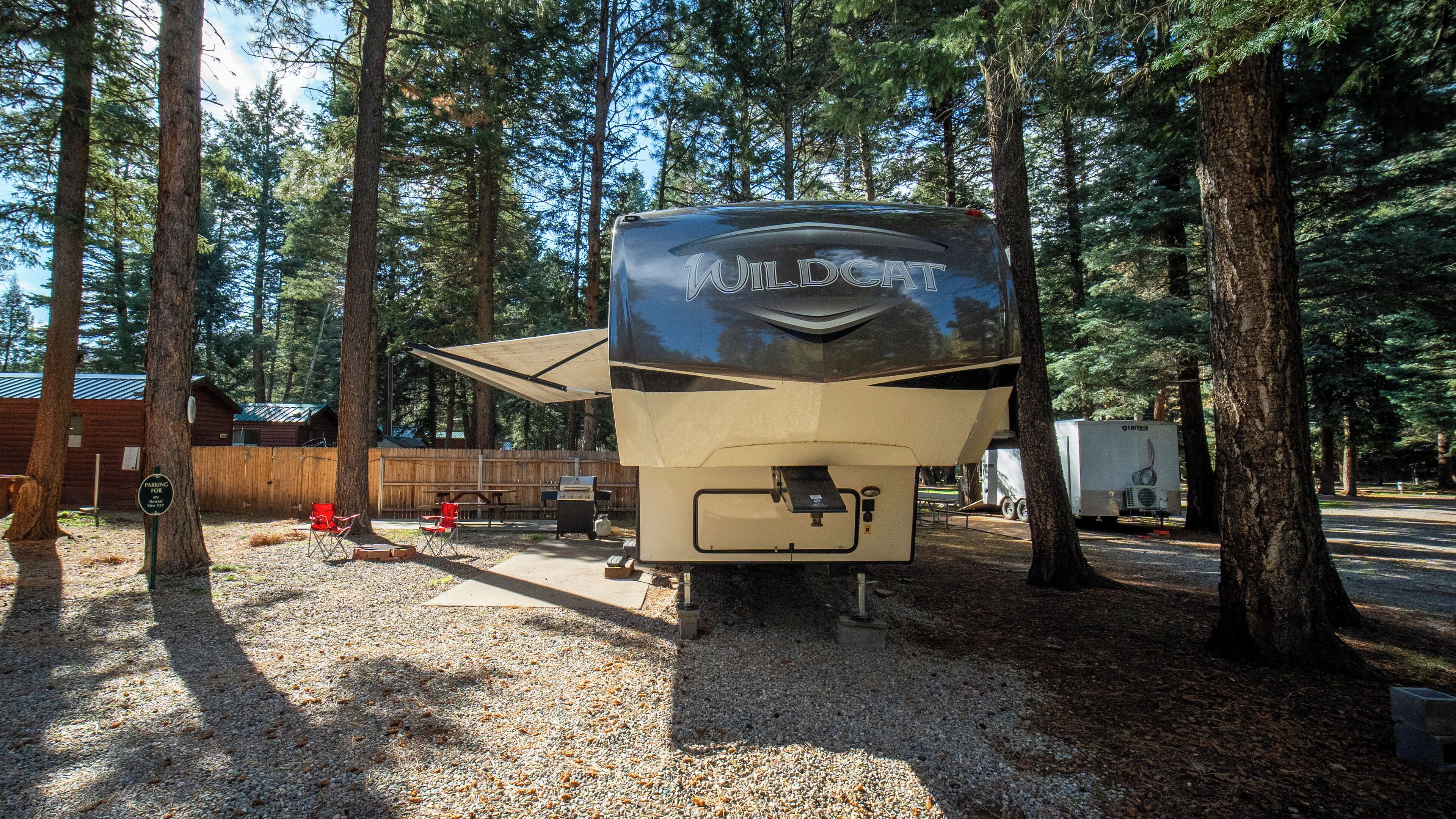 A recreational vehicle (RV) parked in a wooded area with a gravel ground.