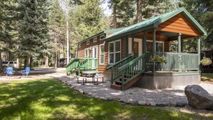 Una cabaña con porche, mobiliario exterior y vistas del bosque circundante.