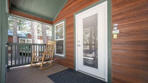 A wooden cabin with a porch, a rocking chair, and a door with a window. - The Twilight Cabin #4 (Bayfield)