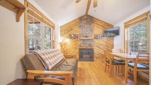 A cozy cabin interior with a fireplace, wooden walls, and a dining area. - The Iris Cabin #1 Sum (Bayfield)