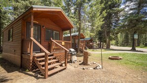 A wooden cabin with a porch, a grill, and a sign indicating it's a campground. - The Willows Cabin #7 (Bayfield)
