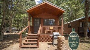 A cabin with a wooden deck, a barbecue grill, and a sign indicating parking for Shooting Star Cabin Site #11. - The Willows Cabin #7 (Bayfield)