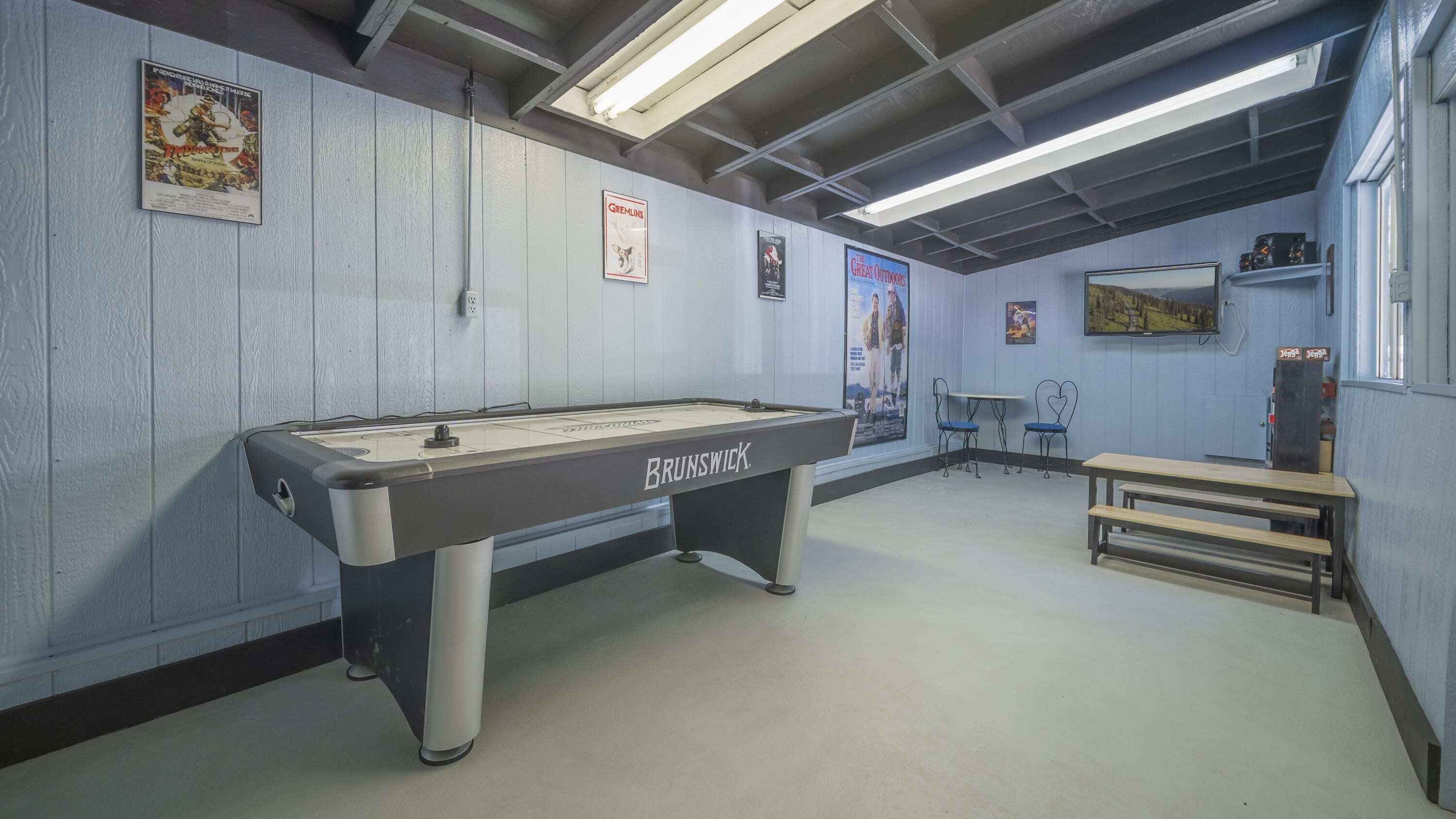 Una mesa de billar con la etiqueta 'BRUNSWICK' en una habitación con paredes azul claro, carteles y una pequeña mesa con sillas.