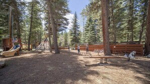 A playground with a slide, a teepee, and a swing set in a wooded area. - The Willows Cabin #7 (Bayfield)