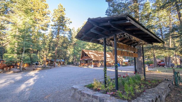 A gravel parking area with a wooden sign indicating 'Blue Spruce RV Park'. - The Willows Cabin #7 (Bayfield)