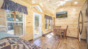 A cozy cabin interior with wooden walls, a dining area with chairs, a table, and a large window. - The Fox Den Cabin #14 (Bayfield)