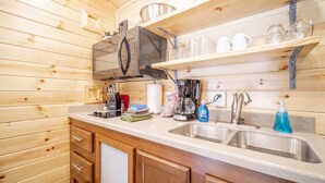A kitchen with wooden walls, a stainless steel sink, a coffee maker, and various kitchen utensils. - The Fox Den Cabin #14 (Bayfield)