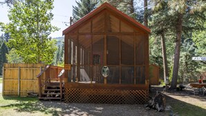 A wooden cabin with a porch, a sign indicating it is a cabin, and a view of the surrounding forest. - The Weminuche Cabin #80 (Bayfield)