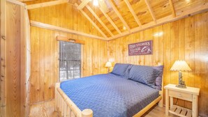 A wooden cabin room with a bed, two bedside lamps, a window with blinds, and a sign on the wall. - The Weminuche Cabin #80 (Bayfield)