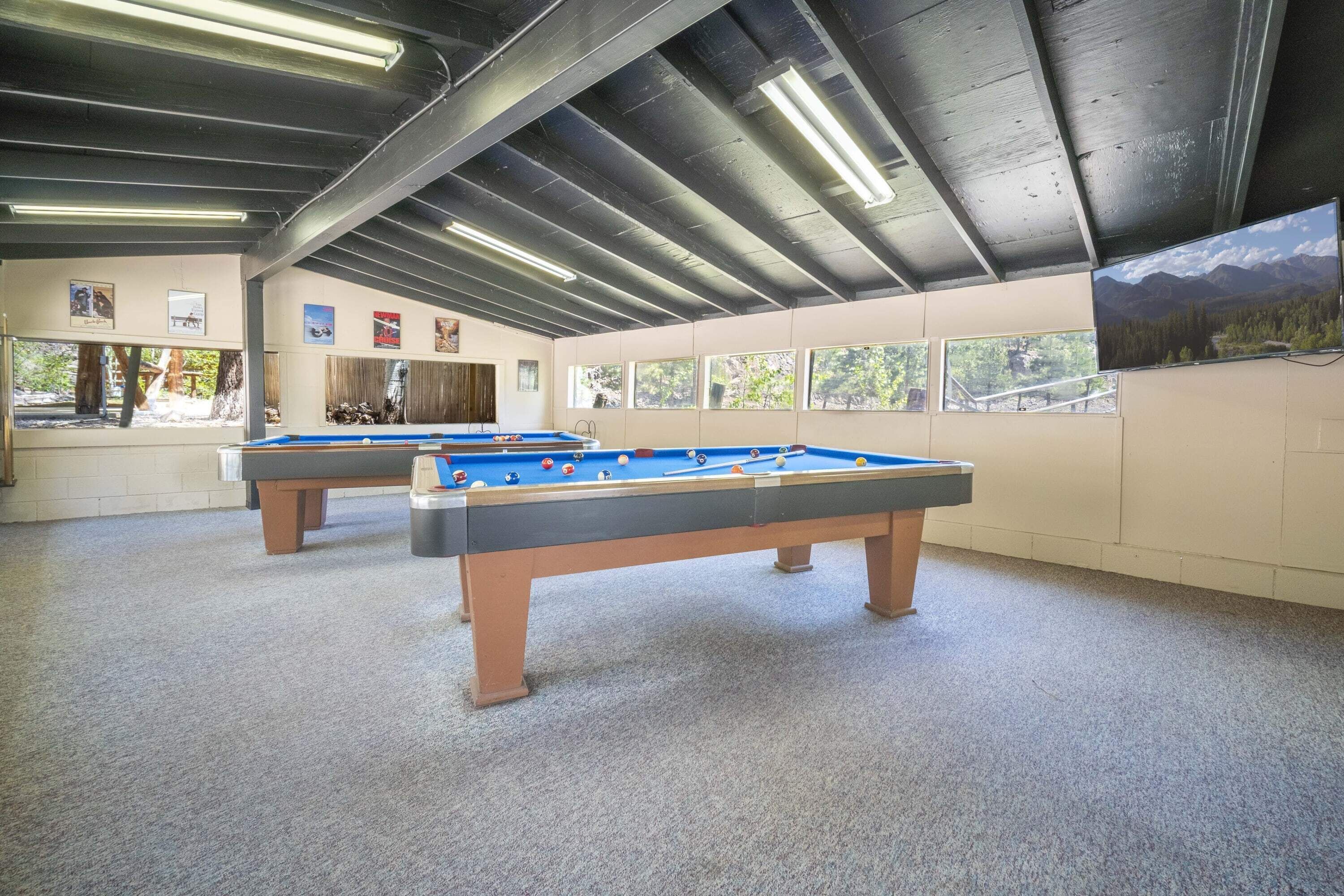 A pool table in a room with a high ceiling and large windows.