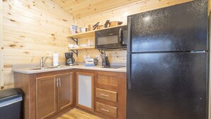 A compact kitchen with wooden walls, a black refrigerator, a microwave, and a coffee maker. - The Shooting Star Cabin #11 (Bayfield)