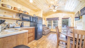 A cozy cabin interior with a kitchen, dining area, and a window overlooking a snowy landscape. - The Shooting Star Cabin #11 (Bayfield)