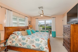 Une chambre avec un lit en bois, une commode, une télévision et un balcon donnant sur une piscine.