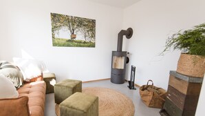 Una sala de estar acogedora con un sofá, otomanas, un tapete tejido, una chimenea, un cuadro y una planta en maceta.